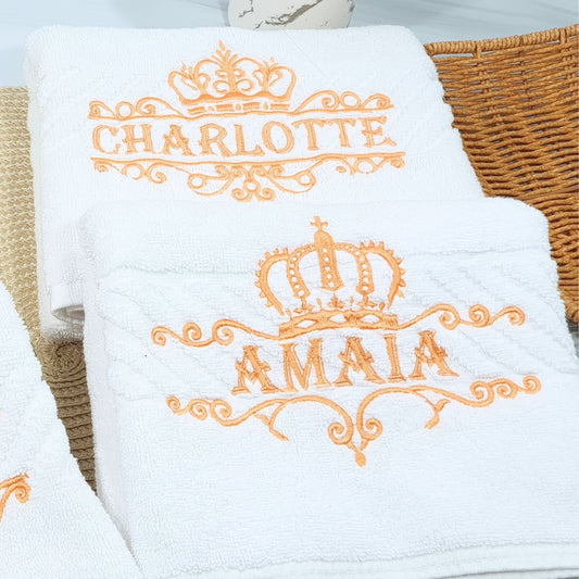 White towels with orange embroidered names and crowns on a woven basket.