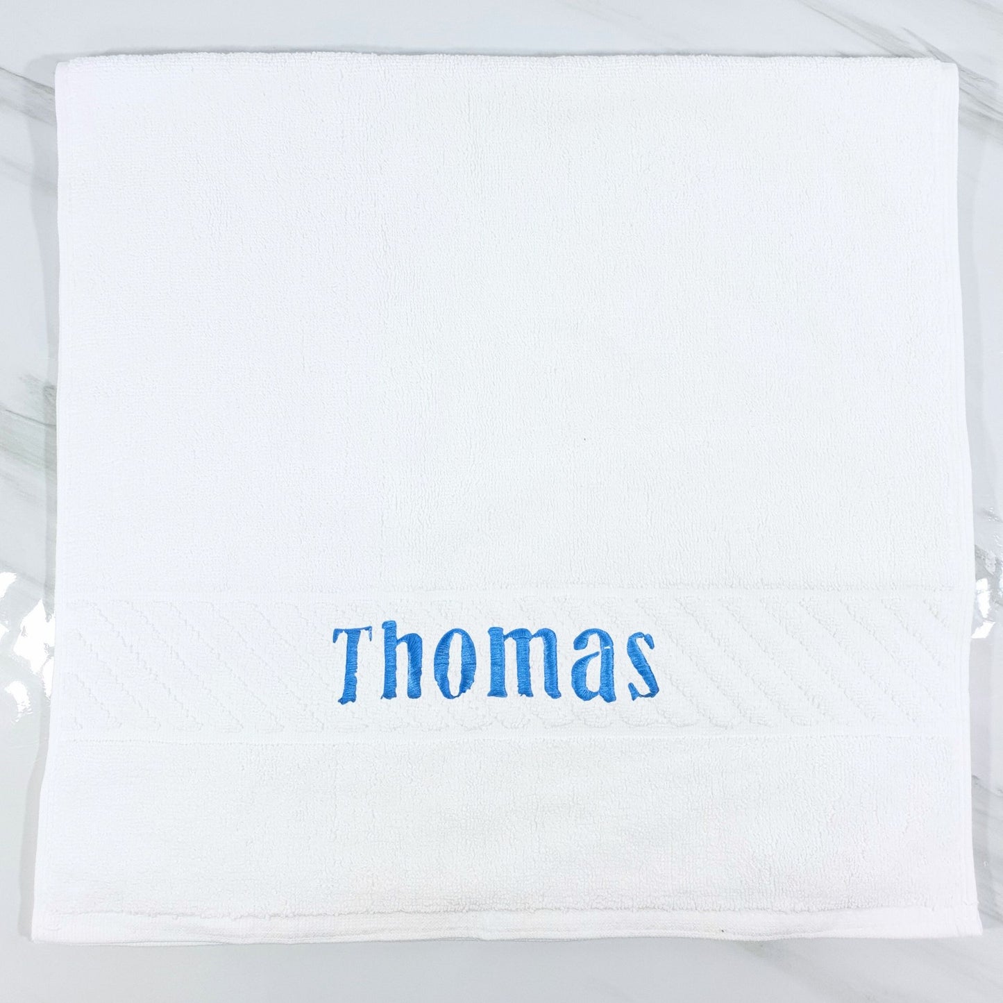 White hand towel with 'Thomas' embroidered in blue on a white background