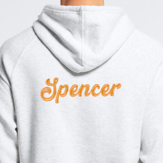 White hoodie with 'Spencer' embroidered on the back in orange.