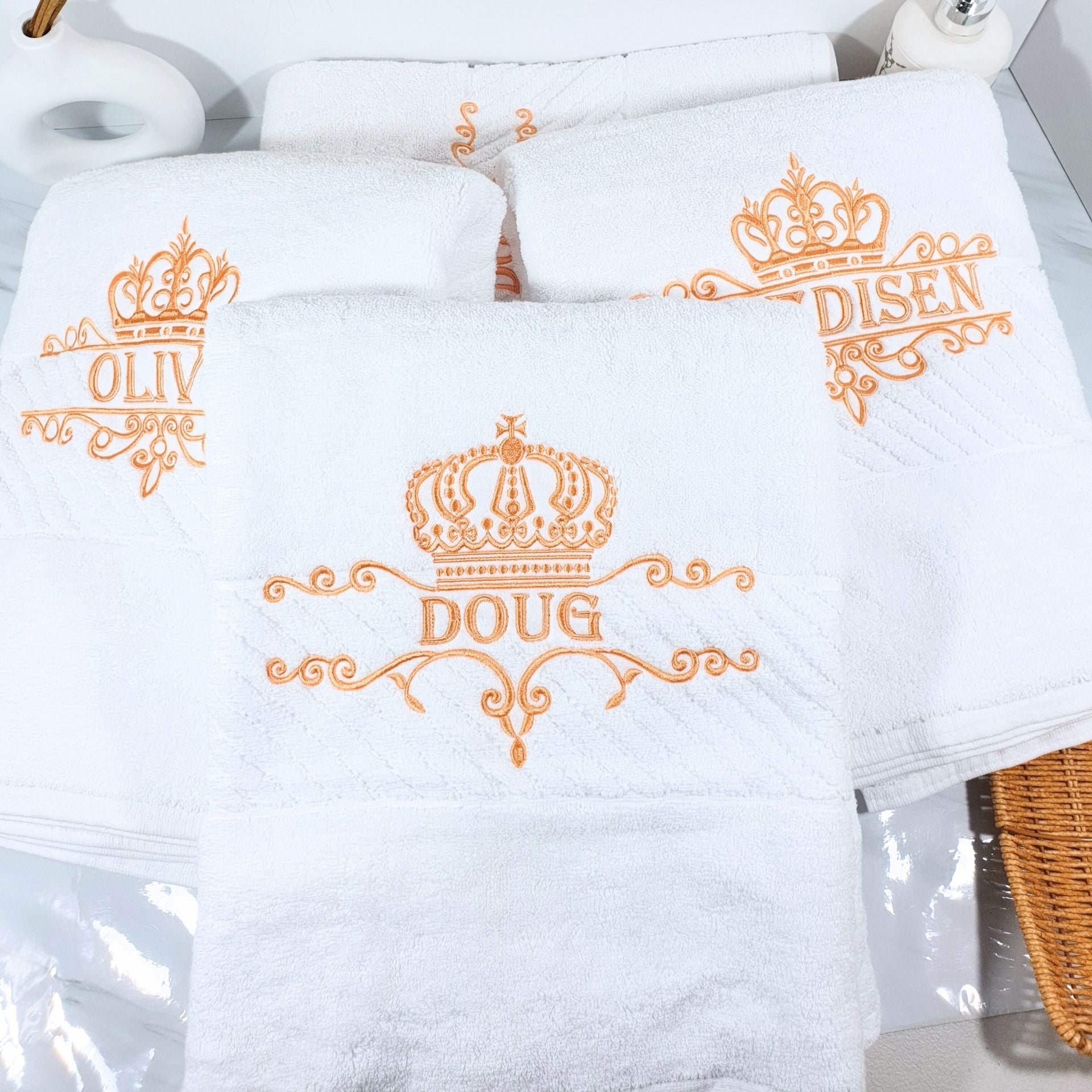 White bath towels with orange embroidered names and crowns on a white background
