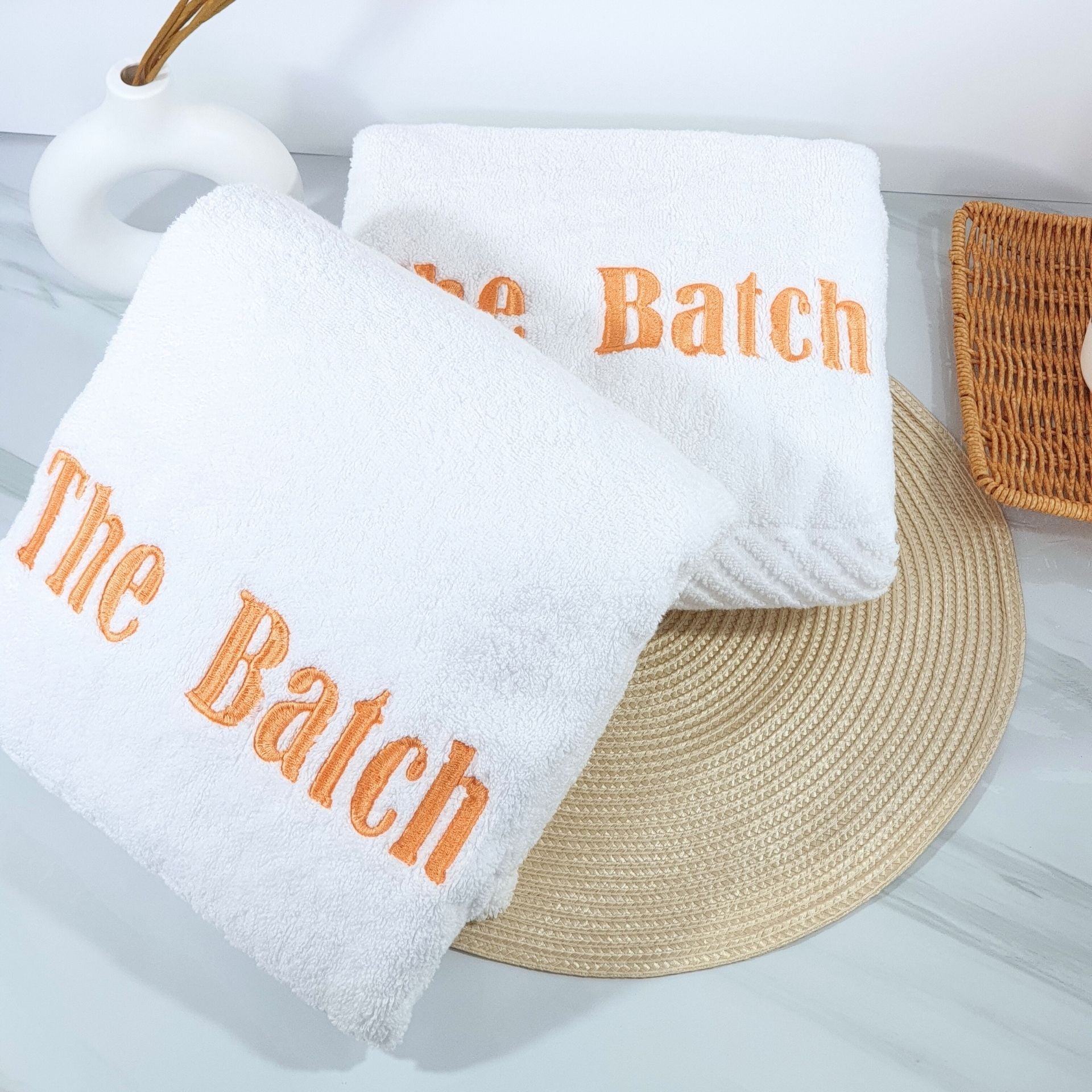 White bath towels with 'The Batch' text on a light gray surface