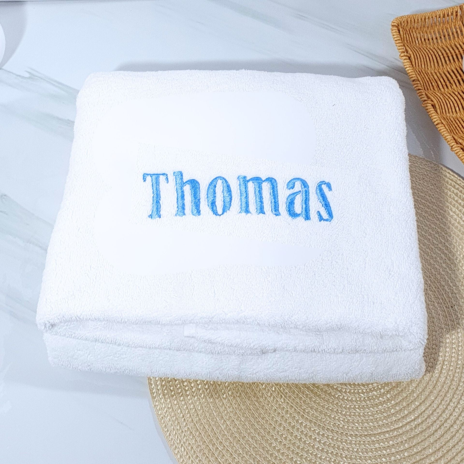 White bath towel with 'Thomas' embroidered in blue on a light gray background