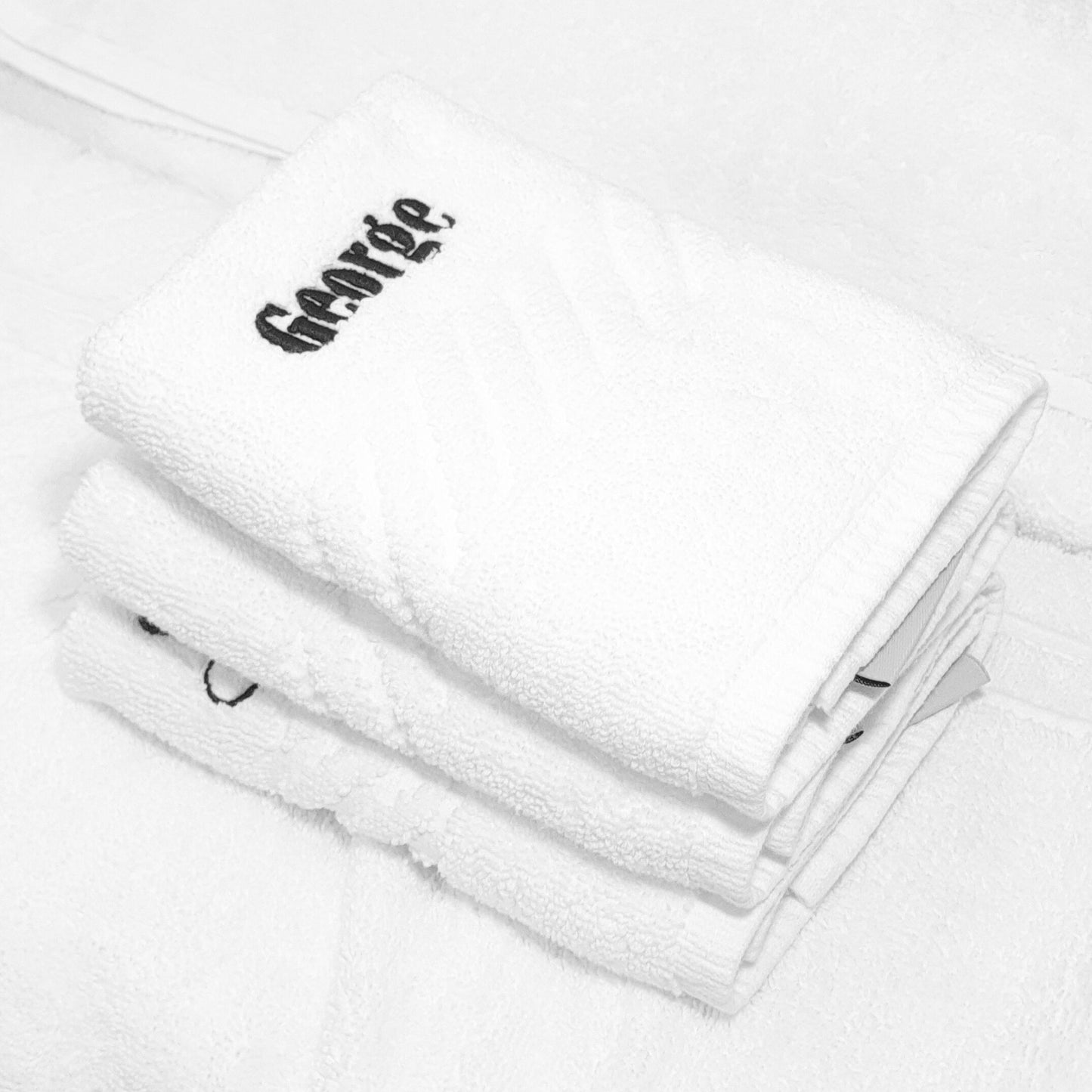 Stack of white towels with embroidered text on a light gray background
