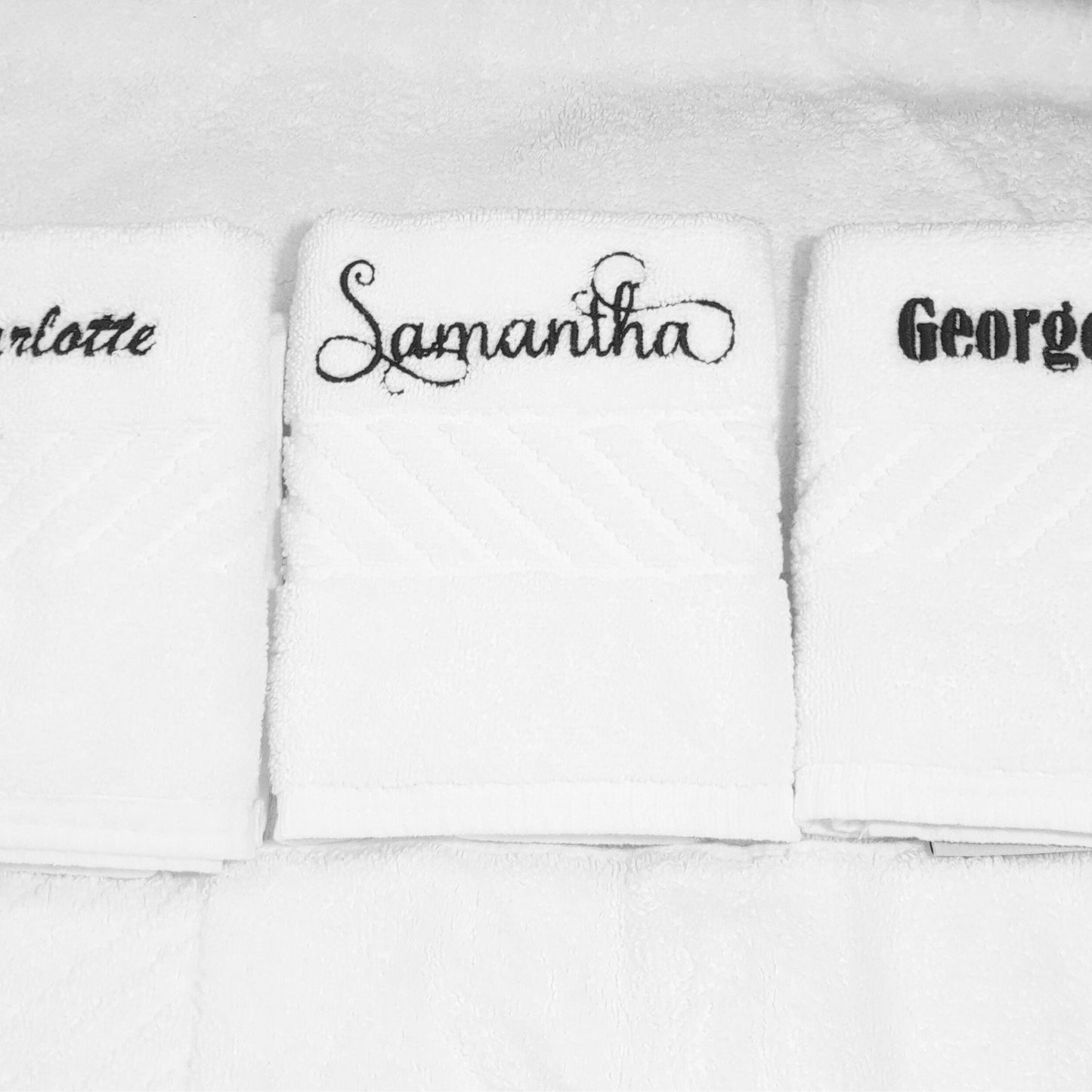 Three white face towels with embroidered names on a white background