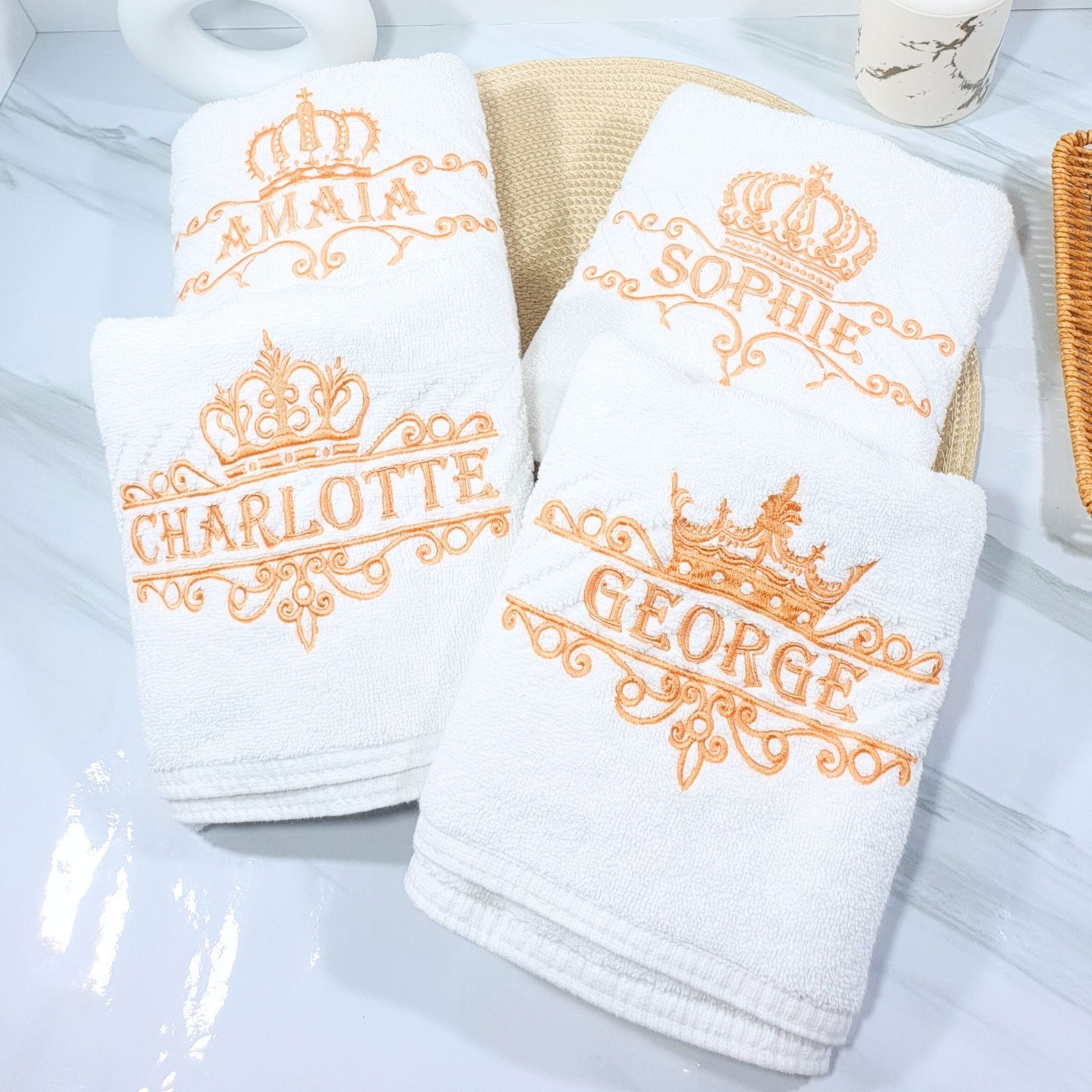 Set of white towels with embroidered names and crowns on a light gray surface.