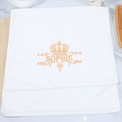 White towel with 'Sophie' and a crown embroidered on it, placed on a white surface.