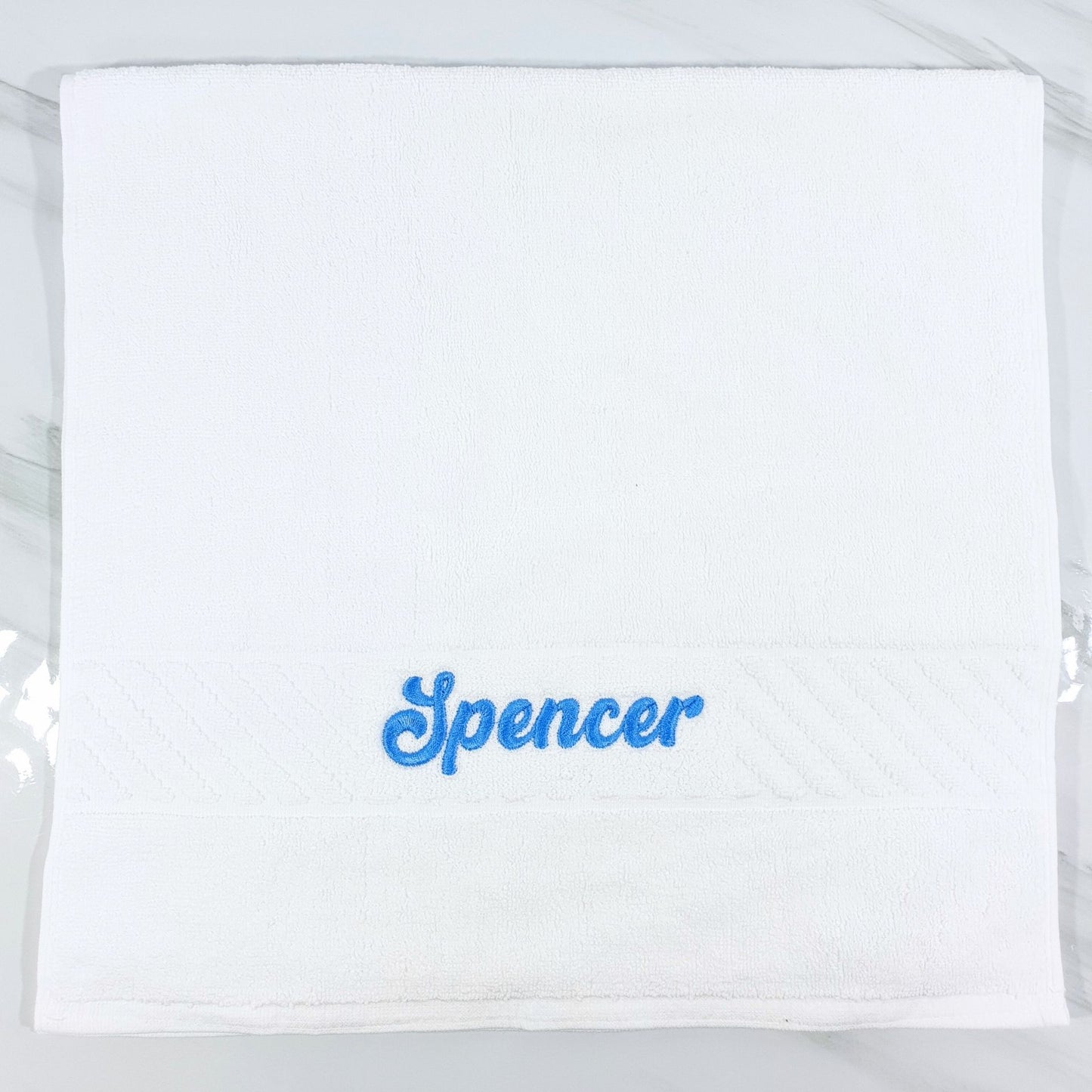 White hand towel with 'Spencer' embroidered in blue on a white background