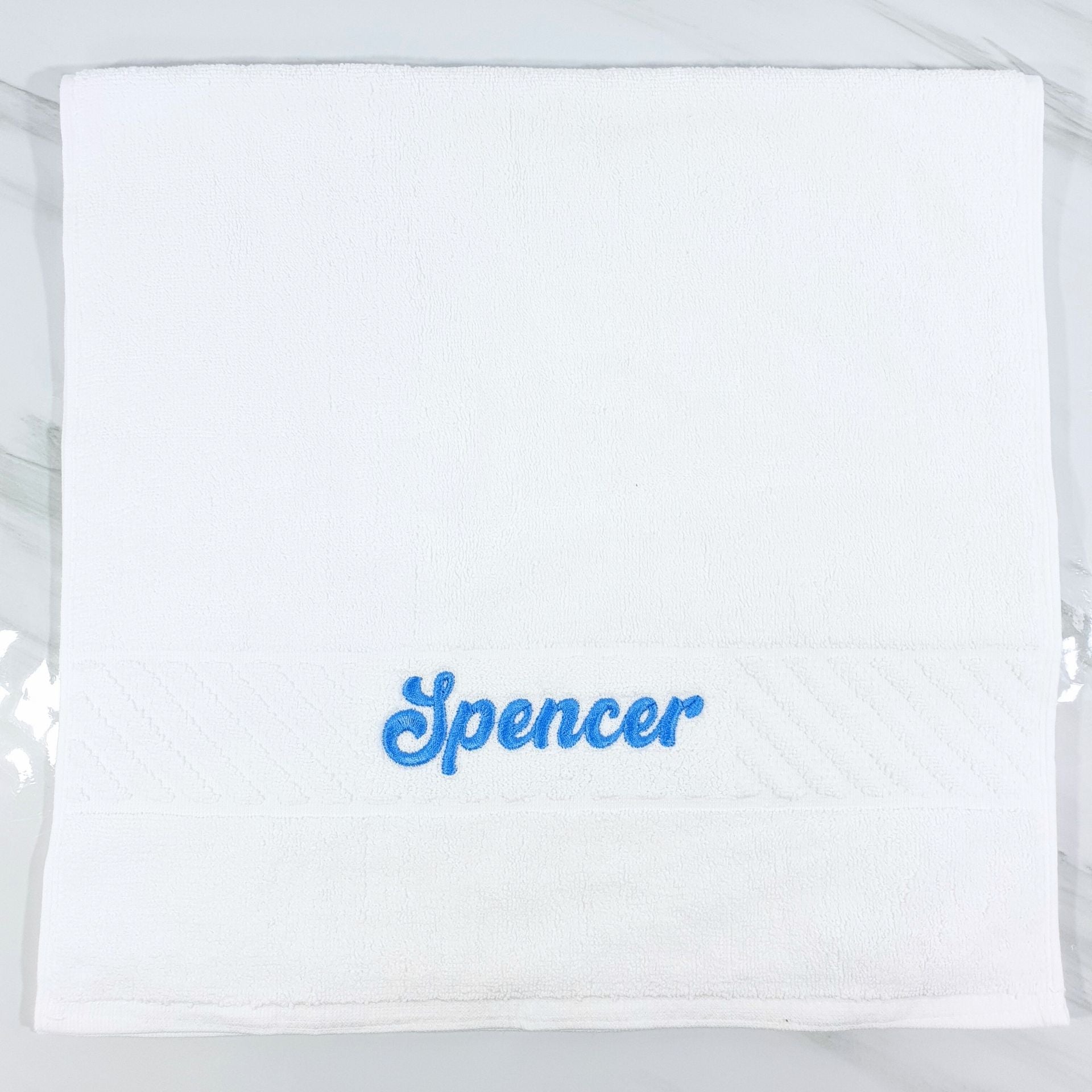 White hand towel with 'Spencer' embroidered in blue on a white background