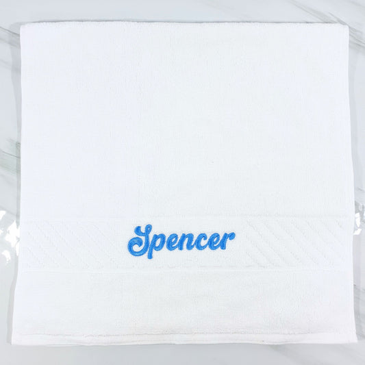 White hand towel with 'Spencer' embroidered in blue on a white background