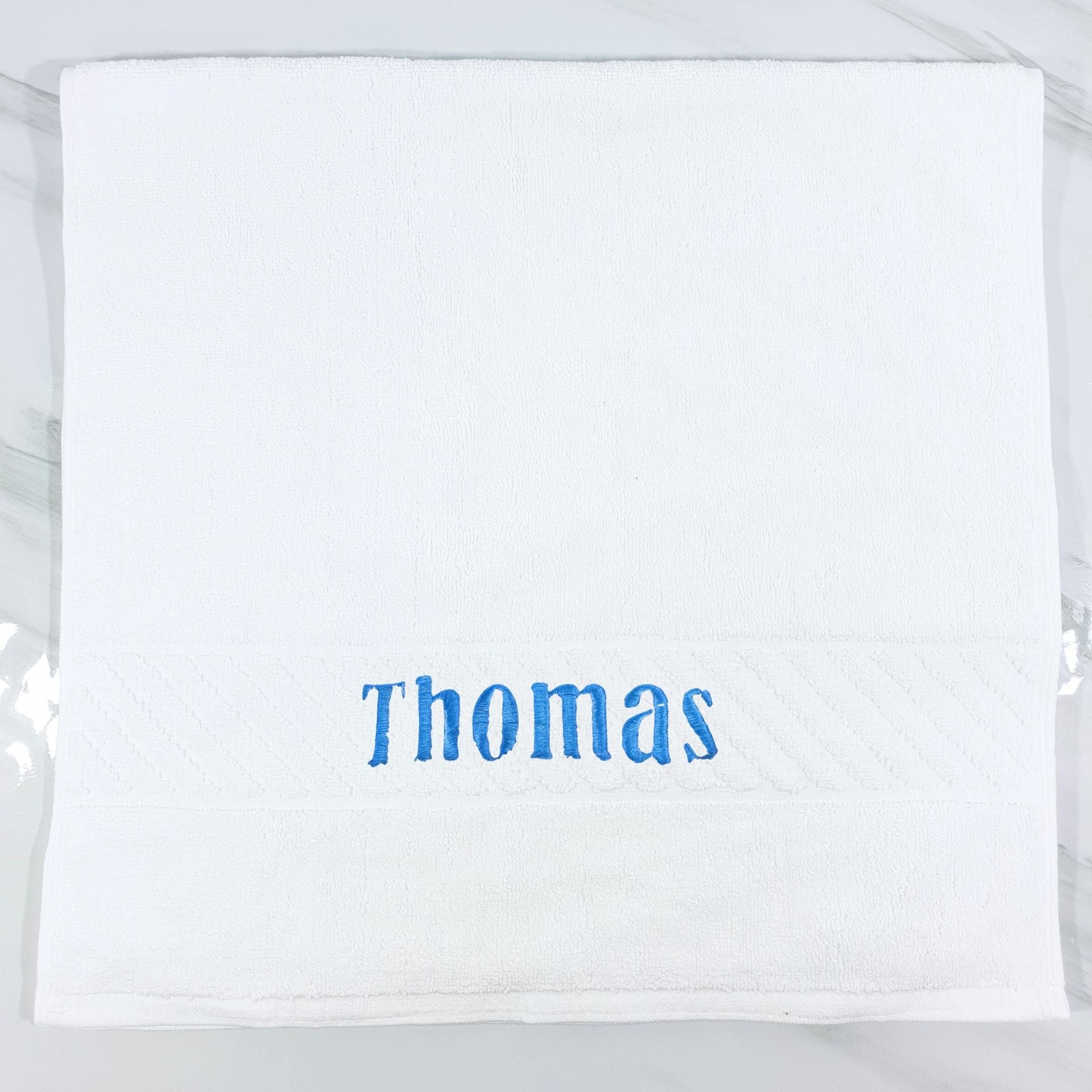 White hand towel with 'Thomas' embroidered in blue on a white background
