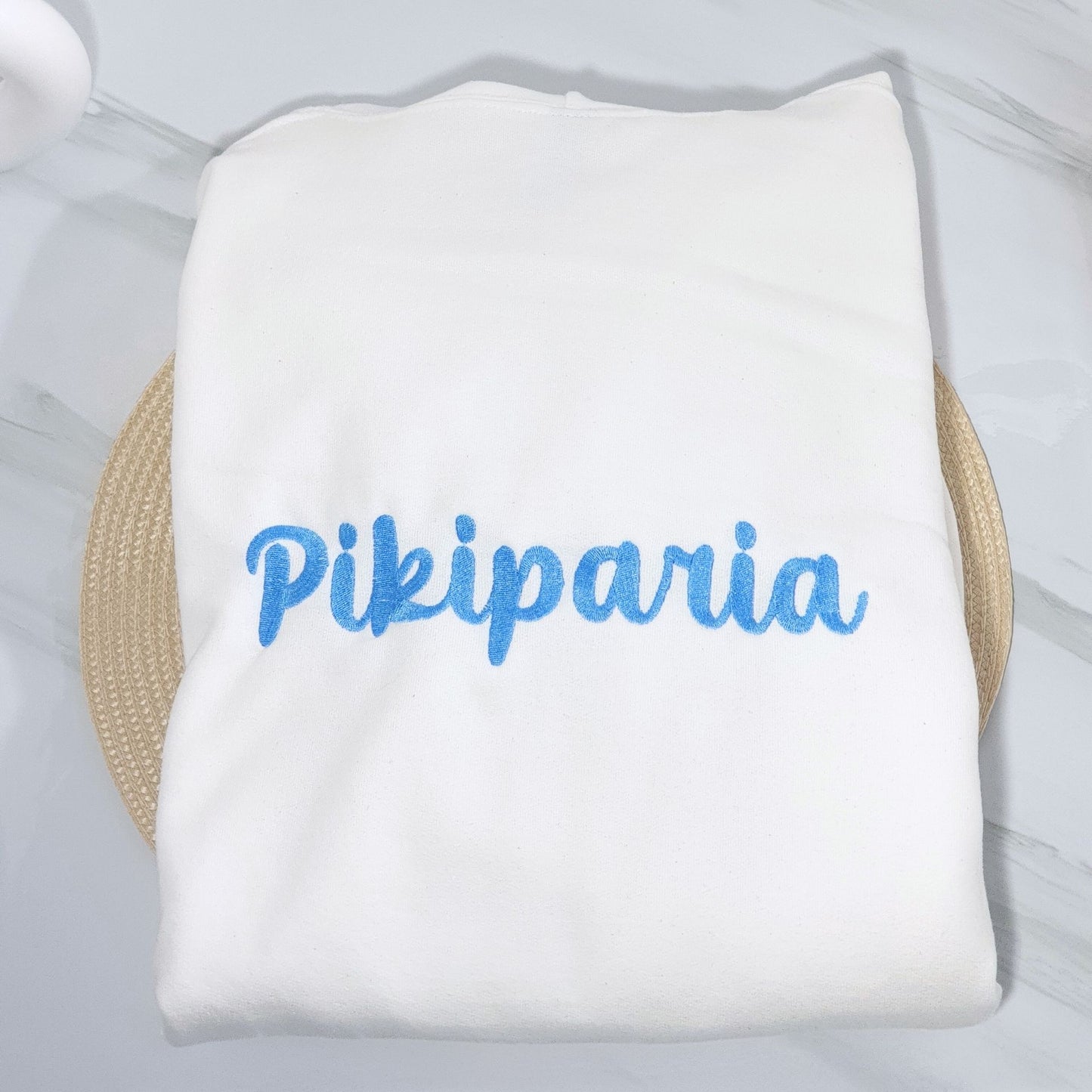 White towel with blue text 'Pikiparia' on a light wooden surface